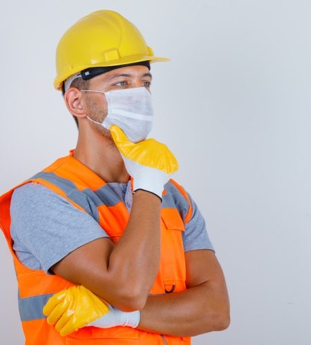 male builder thinking and looking away in uniform, helmet, mask, gloves front view.